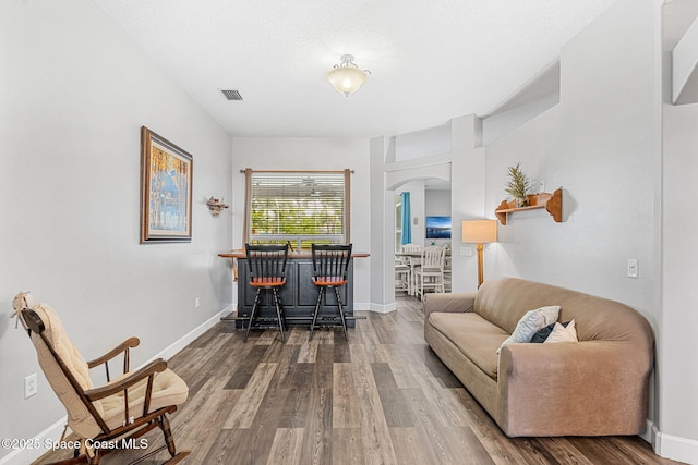 living area with arched walkways, visible vents, baseboards, and wood finished floors