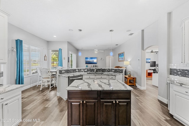 kitchen featuring arched walkways, a ceiling fan, backsplash, light wood finished floors, and an island with sink