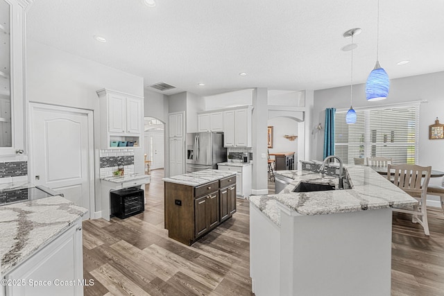 kitchen featuring a sink, stainless steel fridge, a center island with sink, and decorative backsplash