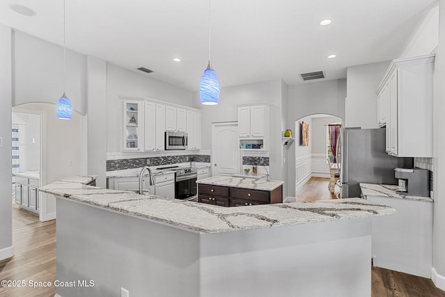 kitchen with arched walkways, visible vents, appliances with stainless steel finishes, backsplash, and a center island