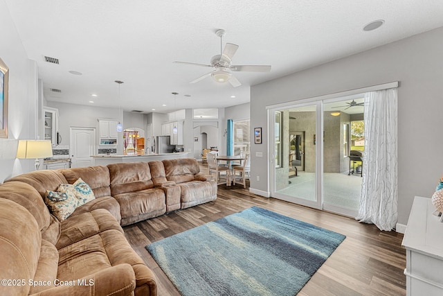 living room featuring a ceiling fan, visible vents, baseboards, and wood finished floors