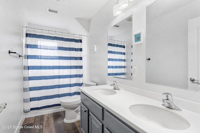 bathroom featuring toilet, double vanity, a sink, and wood finished floors