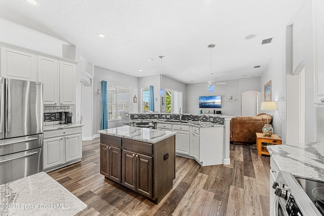 kitchen featuring arched walkways, stainless steel appliances, visible vents, open floor plan, and an island with sink