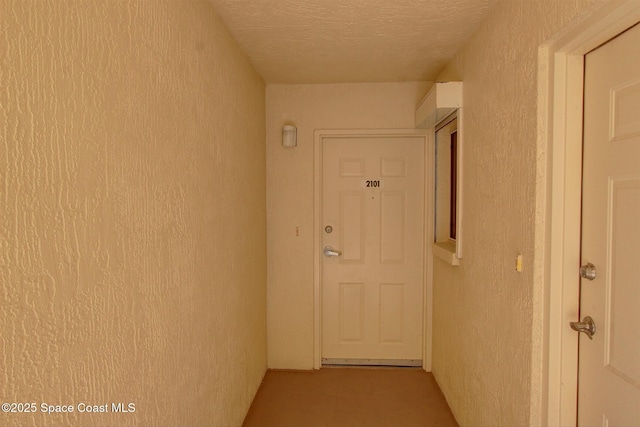 hallway featuring a textured ceiling and a textured wall