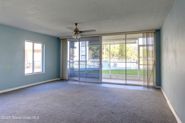 carpeted empty room with a textured ceiling, baseboards, a ceiling fan, and floor to ceiling windows