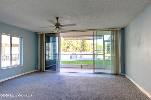 carpeted empty room featuring a textured ceiling, ceiling fan, a wall of windows, and baseboards