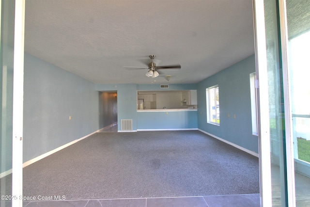 unfurnished living room featuring carpet floors, visible vents, ceiling fan, a textured ceiling, and baseboards