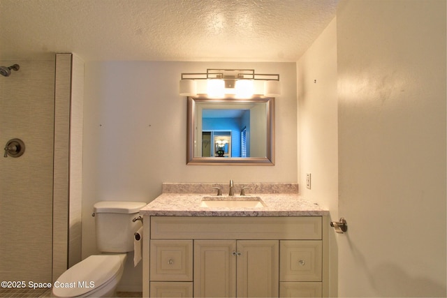 bathroom with a textured ceiling, tiled shower, vanity, and toilet