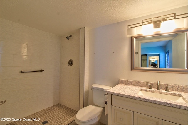 bathroom with a textured ceiling, vanity, a tile shower, and toilet