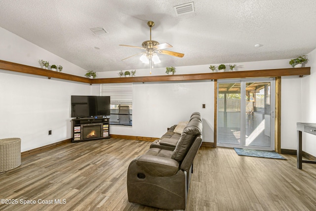 living room featuring lofted ceiling, visible vents, a glass covered fireplace, and wood finished floors