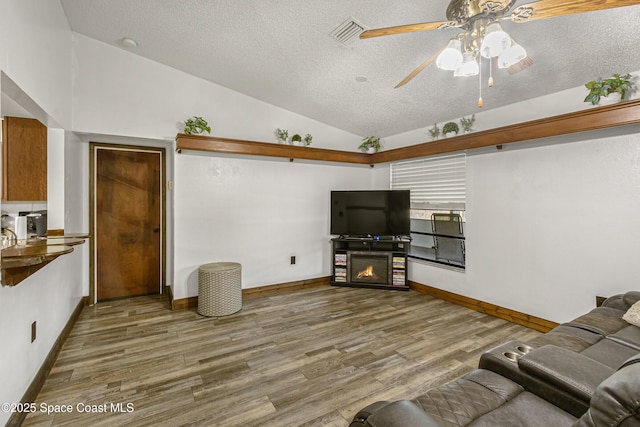 living area featuring lofted ceiling, visible vents, a textured ceiling, and wood finished floors