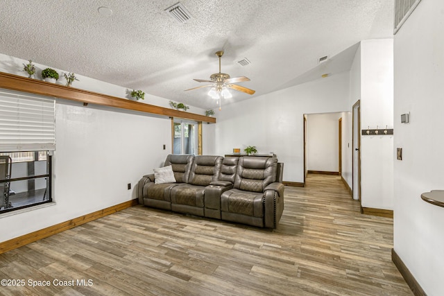 living area with lofted ceiling, a textured ceiling, wood finished floors, and visible vents