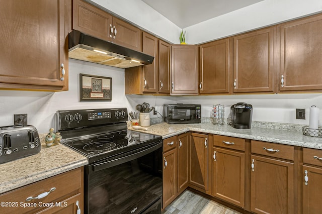 kitchen with light stone countertops, black appliances, under cabinet range hood, and brown cabinetry