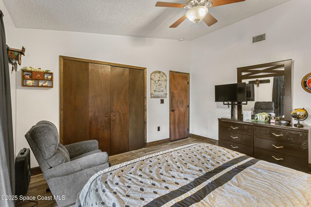 bedroom with visible vents, wood finished floors, vaulted ceiling, a textured ceiling, and a closet