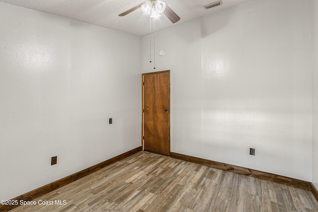 empty room featuring a textured ceiling, wood finished floors, a ceiling fan, visible vents, and baseboards