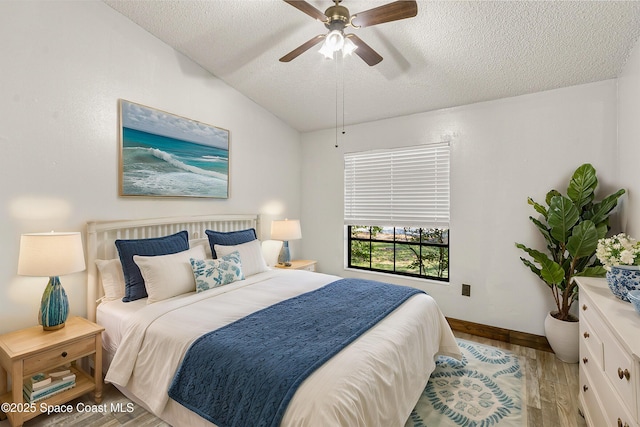 bedroom with ceiling fan, vaulted ceiling, a textured ceiling, wood finished floors, and baseboards