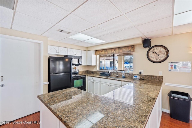 kitchen featuring a peninsula, a sink, visible vents, white cabinets, and black appliances