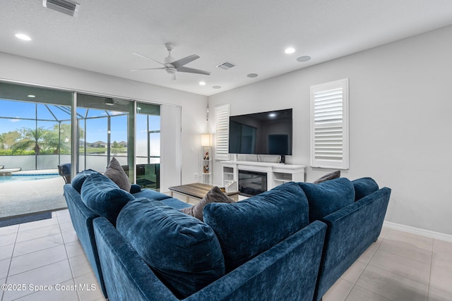 living room featuring light tile patterned floors, a glass covered fireplace, and visible vents