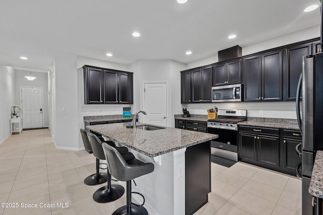 kitchen featuring stainless steel appliances, stone countertops, light tile patterned flooring, a sink, and an island with sink