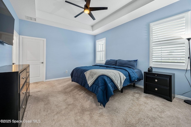 carpeted bedroom with a tray ceiling, visible vents, ceiling fan, and baseboards