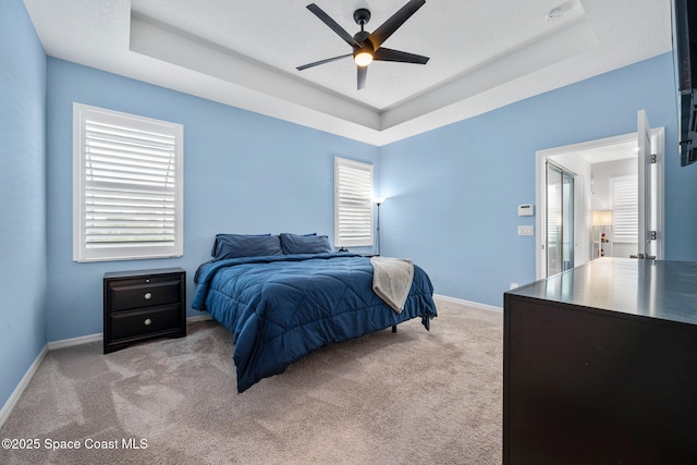 bedroom featuring light carpet, a tray ceiling, a ceiling fan, and baseboards