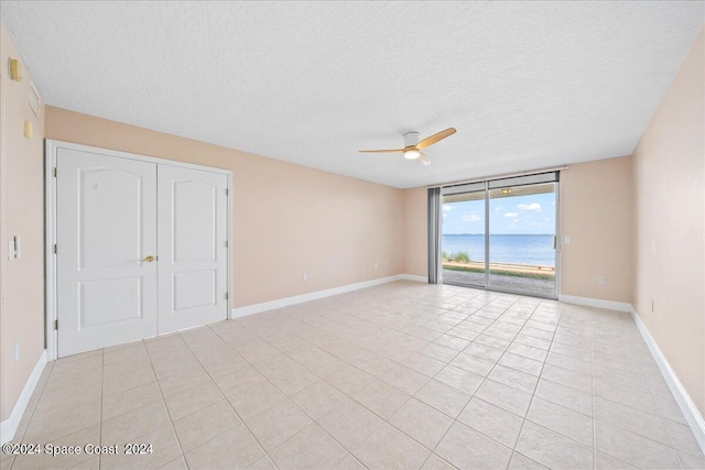 spare room featuring baseboards, ceiling fan, a water view, a textured ceiling, and floor to ceiling windows