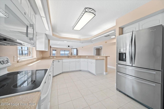 kitchen with a peninsula, white appliances, white cabinetry, and a tray ceiling