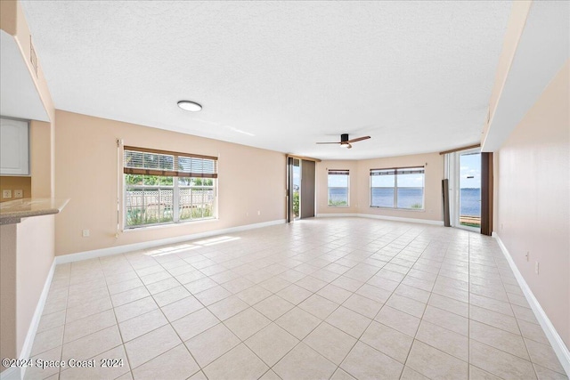 unfurnished living room with a textured ceiling, a ceiling fan, a wealth of natural light, and light tile patterned flooring