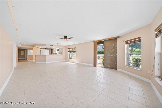 unfurnished living room with baseboards, light tile patterned flooring, a wealth of natural light, and a ceiling fan