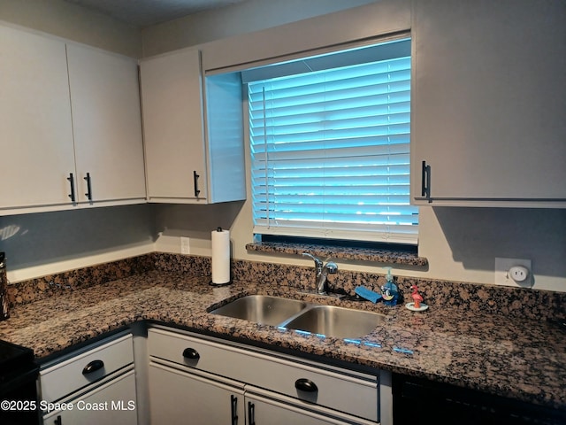 kitchen with dark stone countertops, a sink, and white cabinetry