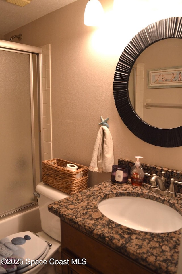 full bath with combined bath / shower with glass door, a textured wall, vanity, and toilet