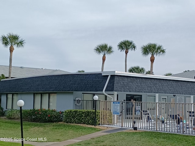 view of front of property featuring mansard roof, roof with shingles, fence, and stucco siding