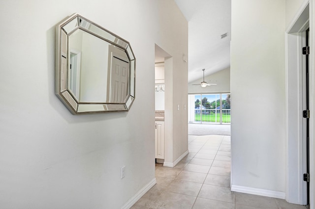 corridor with lofted ceiling, visible vents, baseboards, and light tile patterned floors