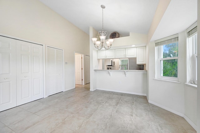 kitchen with high vaulted ceiling, baseboards, light countertops, decorative light fixtures, and an inviting chandelier