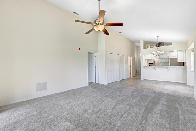 unfurnished living room with light carpet, high vaulted ceiling, ceiling fan with notable chandelier, and visible vents