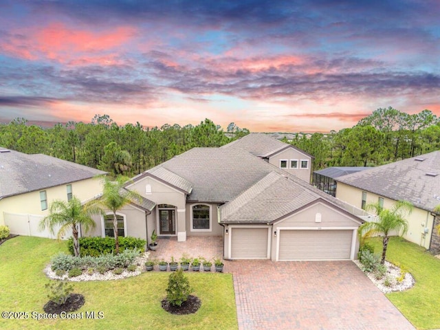 view of front of property with decorative driveway, stucco siding, an attached garage, fence, and a front lawn