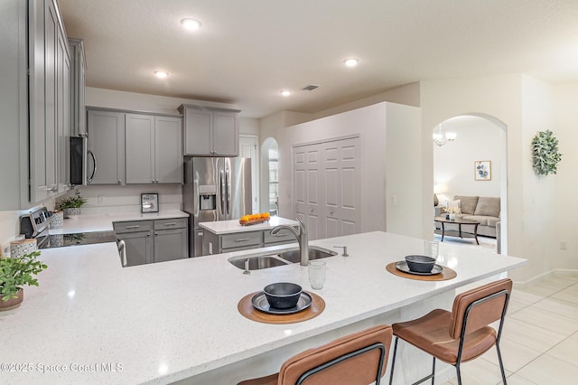 kitchen featuring arched walkways, stainless steel appliances, a sink, and gray cabinetry