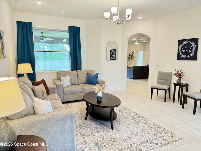 tiled living area with arched walkways, ceiling fan with notable chandelier, and baseboards