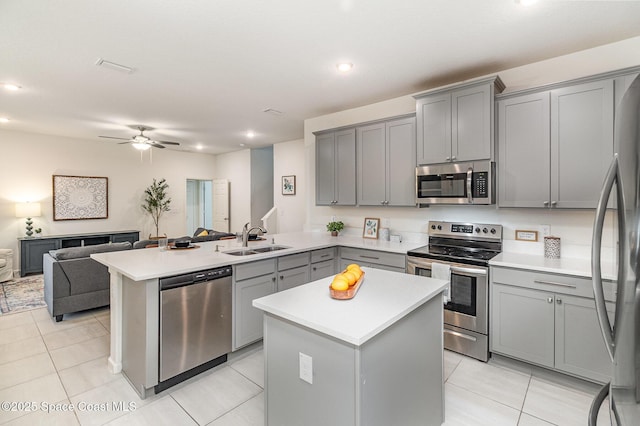 kitchen featuring stainless steel appliances, gray cabinets, open floor plan, a sink, and a peninsula