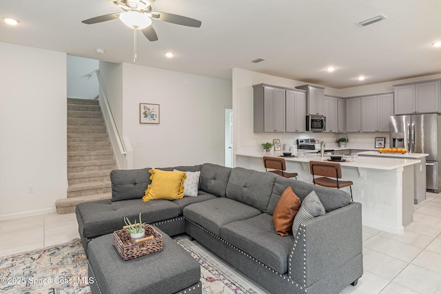 living area with light tile patterned floors, visible vents, stairway, and a ceiling fan