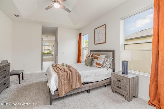 bedroom with a tray ceiling, light colored carpet, visible vents, and multiple windows