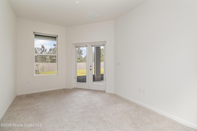 spare room featuring french doors, light carpet, and baseboards