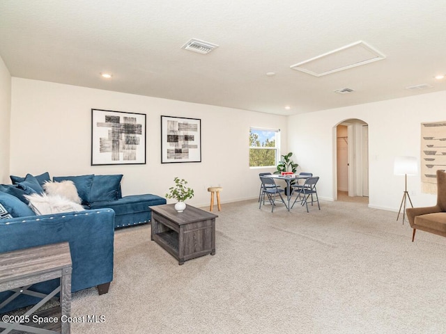 carpeted living area with arched walkways, recessed lighting, visible vents, baseboards, and attic access