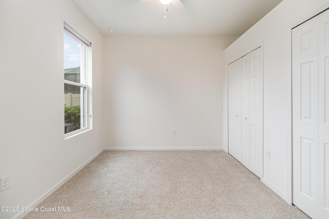 unfurnished bedroom with carpet floors, multiple windows, baseboards, and a ceiling fan