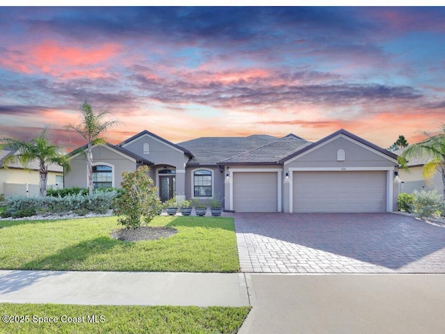 single story home with a garage, decorative driveway, a front yard, and stucco siding