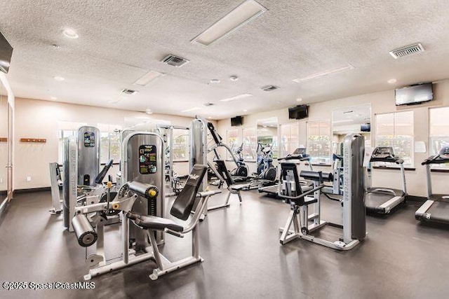 exercise room with baseboards, visible vents, and a textured ceiling