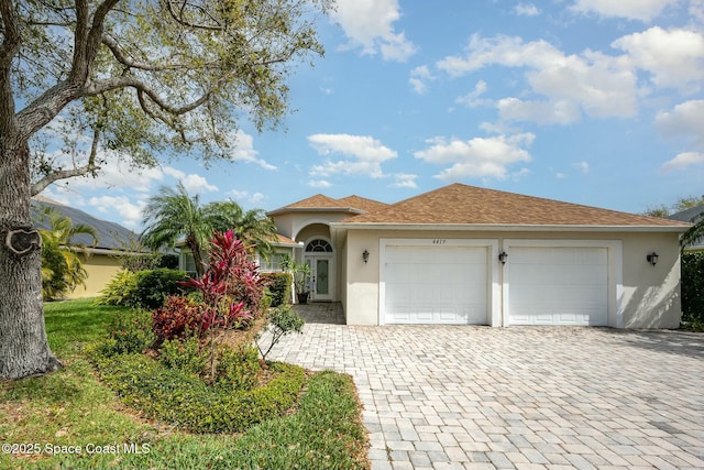 view of front of property featuring an attached garage, roof with shingles, decorative driveway, and stucco siding