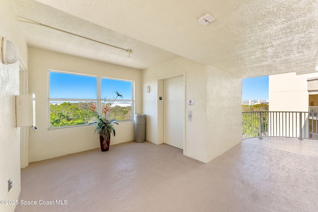 unfurnished room with concrete flooring, elevator, and a textured ceiling