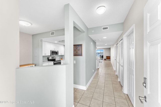 hallway with light tile patterned floors, a textured ceiling, visible vents, and baseboards