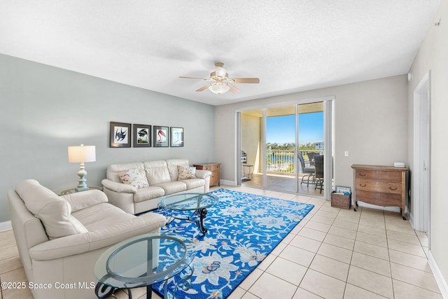 living area with light tile patterned floors, a textured ceiling, a ceiling fan, and baseboards